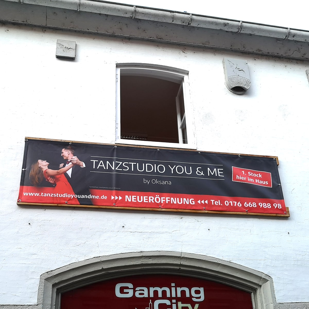 Teaser Quadrat verlinkt, Werbebanner Großformat zur Neueröffnung an weißer Hauswand für Tanzstudio You & Me; Motiv in rot-schwarz zeigt tanzendes Paar, Logo, Infos zu Ort und Kontaktdaten