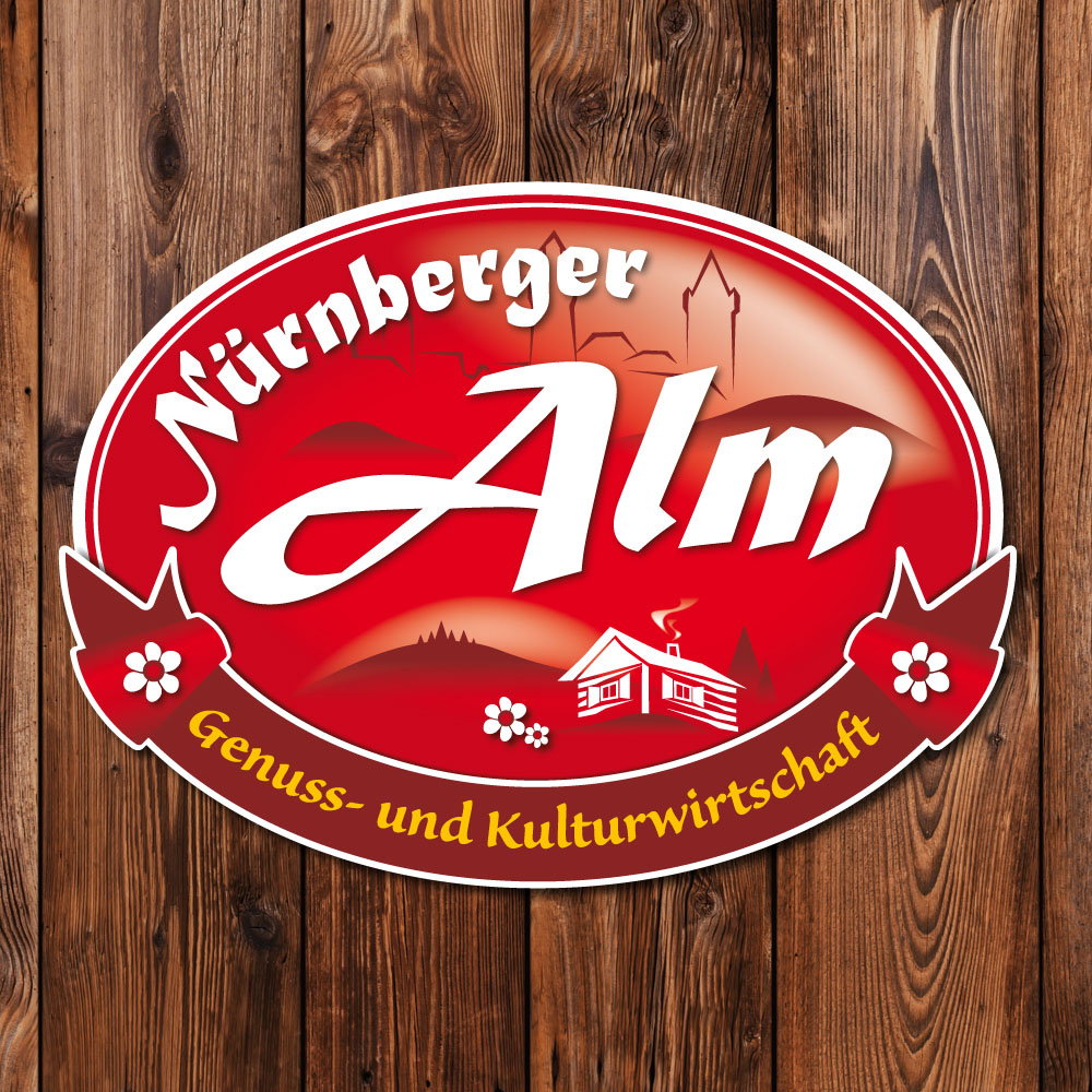Logo Nürnberger Alm; Form Oval quer, Anmutung emailliertes Schild mit Almlandschaft in dunklen Rottönen, weißer Almhütte, Edelweiß und Nürnberger Burg als Silhouette angedeutet; hinter dem Schild rustikale Holzwand